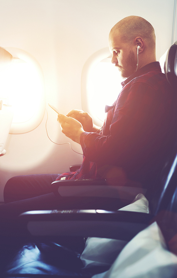 Man using his smart phone with headphones on an airplane